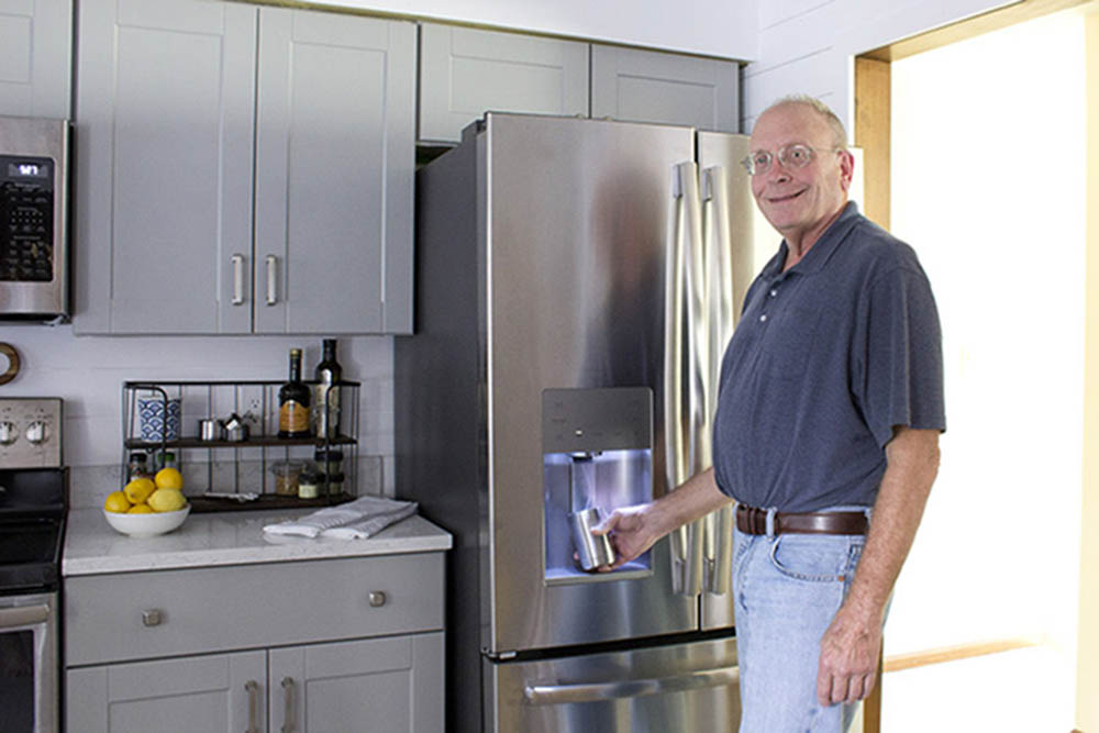 A man gets ice from an in-door ice maker on a GE stainless steel refrigerator.