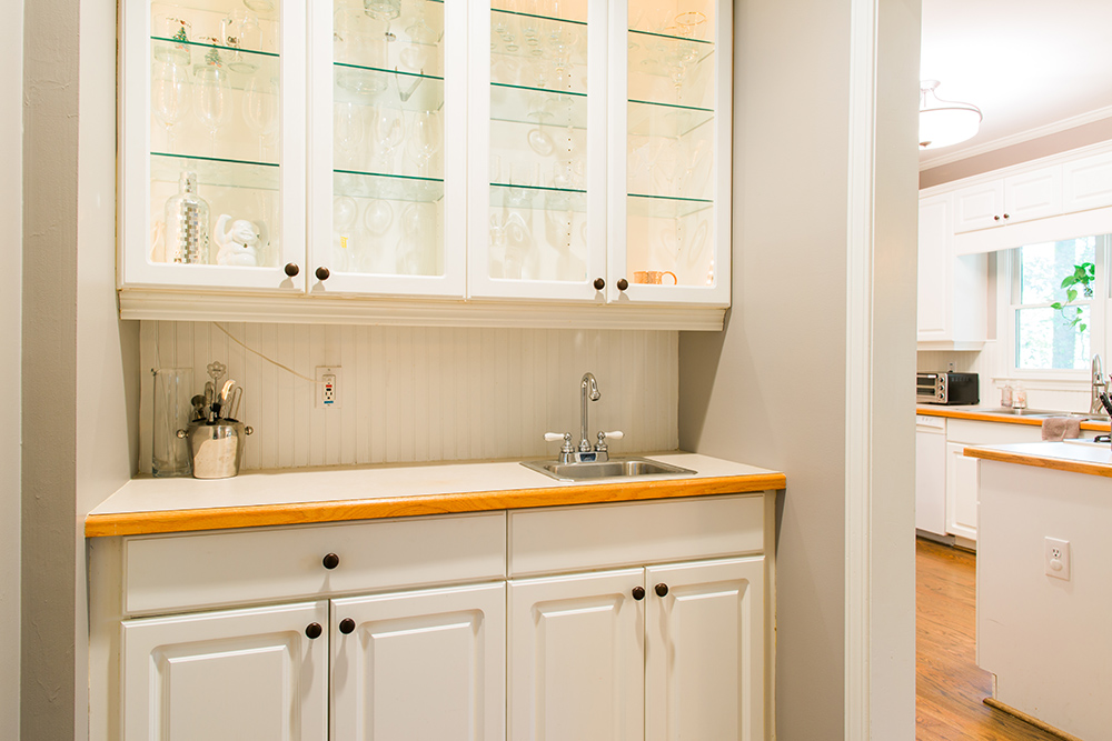 A wall of white open cabinets with glass fronts over a small sink.