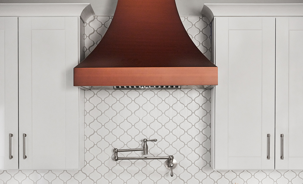 A copper kitchen vent hood installed in subway tile backsplash..