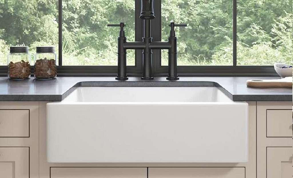 A black faucet installed over a farmhouse sink in a kitchen.