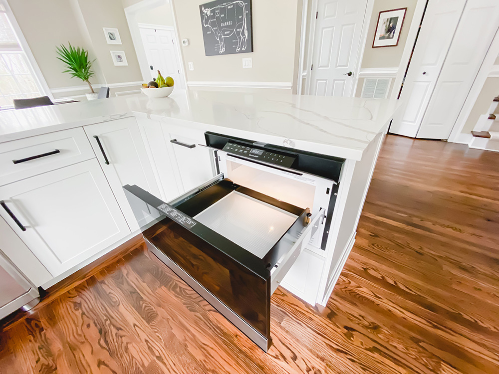 A drawer microwave opens over hardwood flooring.