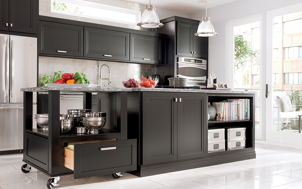 A kitchen with dark colored cabinets and a kitchen island cart with wheels.