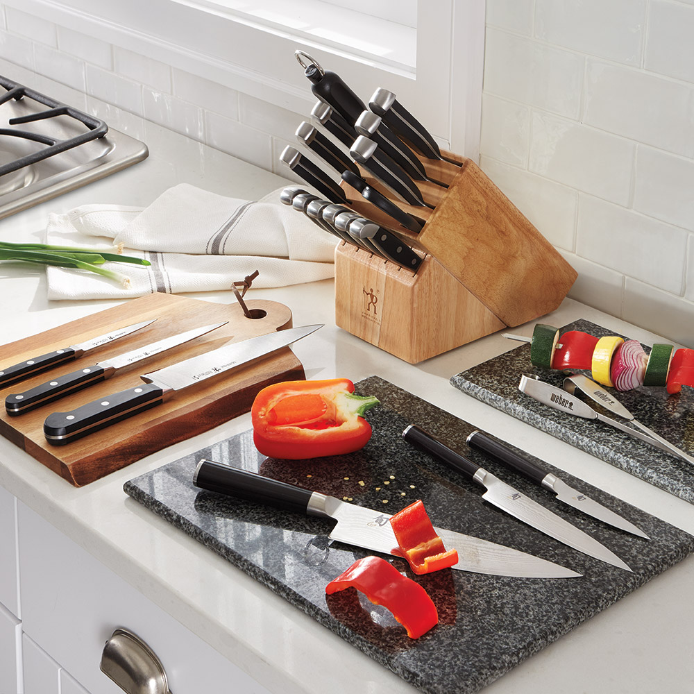 A variety of kitchen knives and a wooden storage block sit on a countertop.