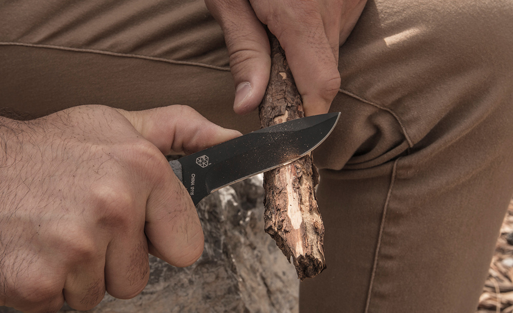 A person uses a hunting knife to sharpen a stick.