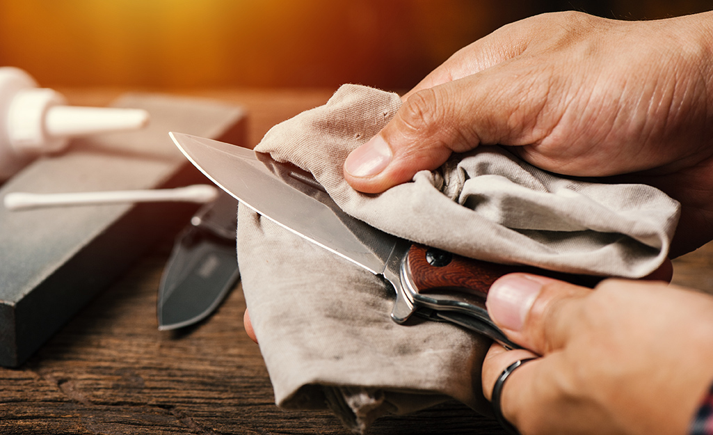 A person uses a cloth to clean the blade of pocket knife.