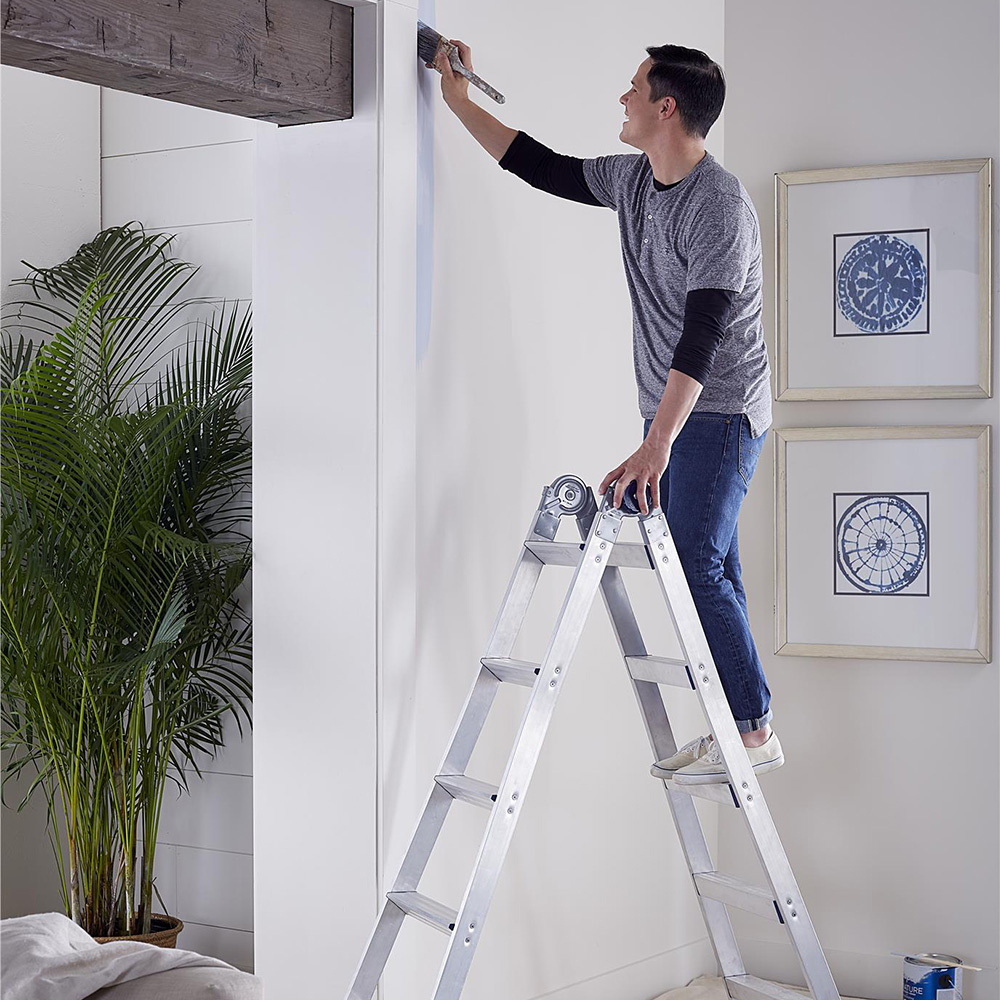 A man on a ladder painting a wall.