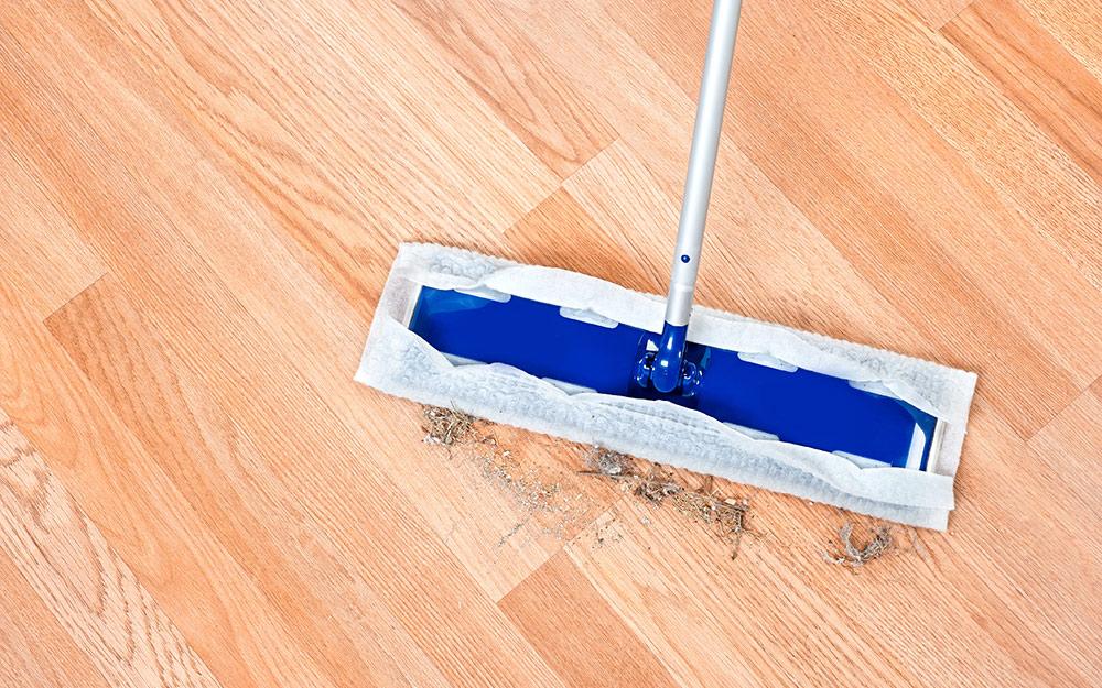 A cleaning tool removing dirt from a light wood-colored laminate floor.