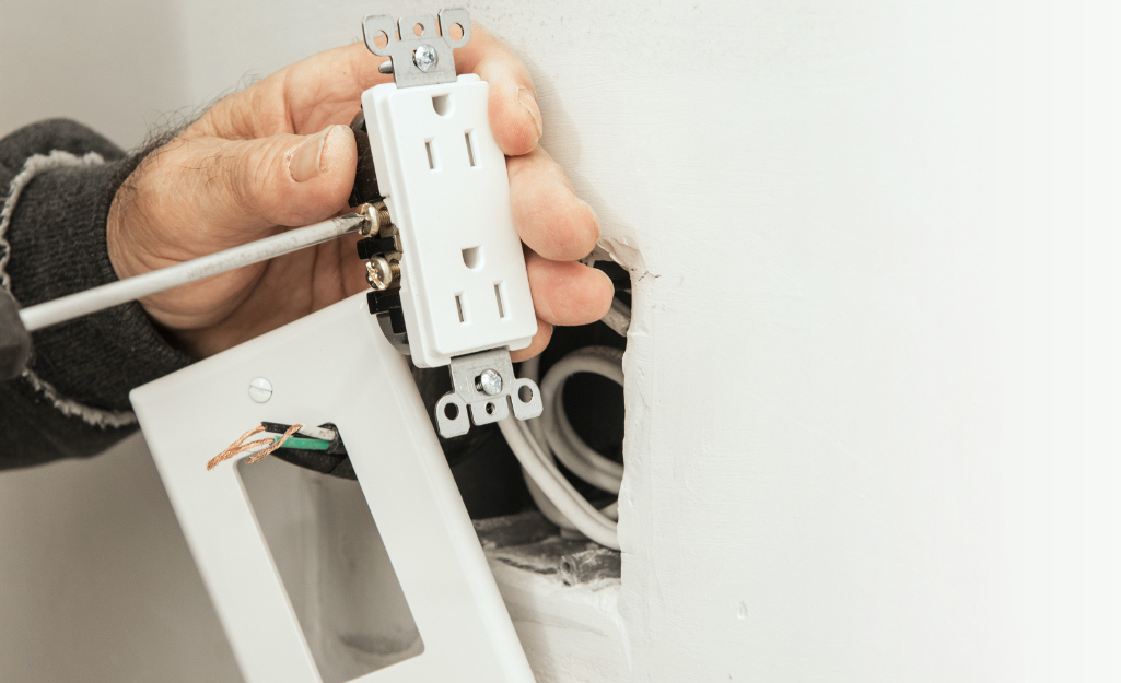 A person installs an electrical outlet in a wall.