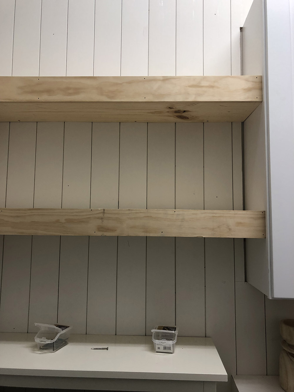 A wall with white vertical shiplap and two floating shelves.