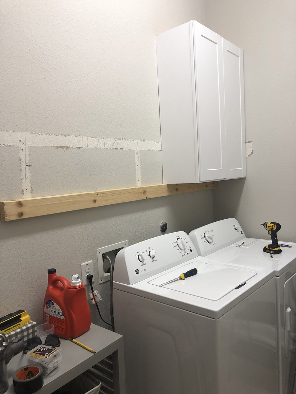 A laundry room with white wall cabinets being installed.