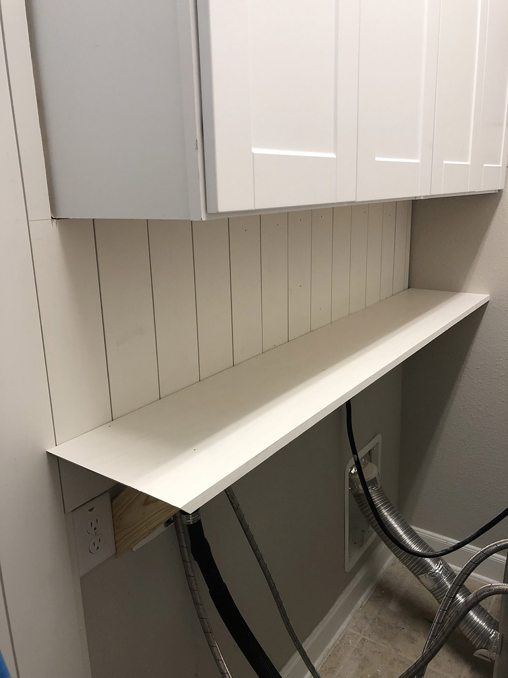 A laundry room wall with a shelf supported by four angled wood supports.