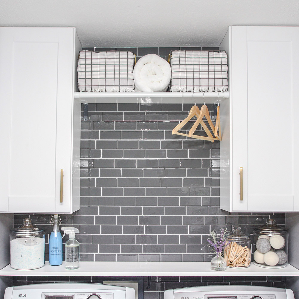 A laundry room with white cabinets and a gray peel and stick tile wall.