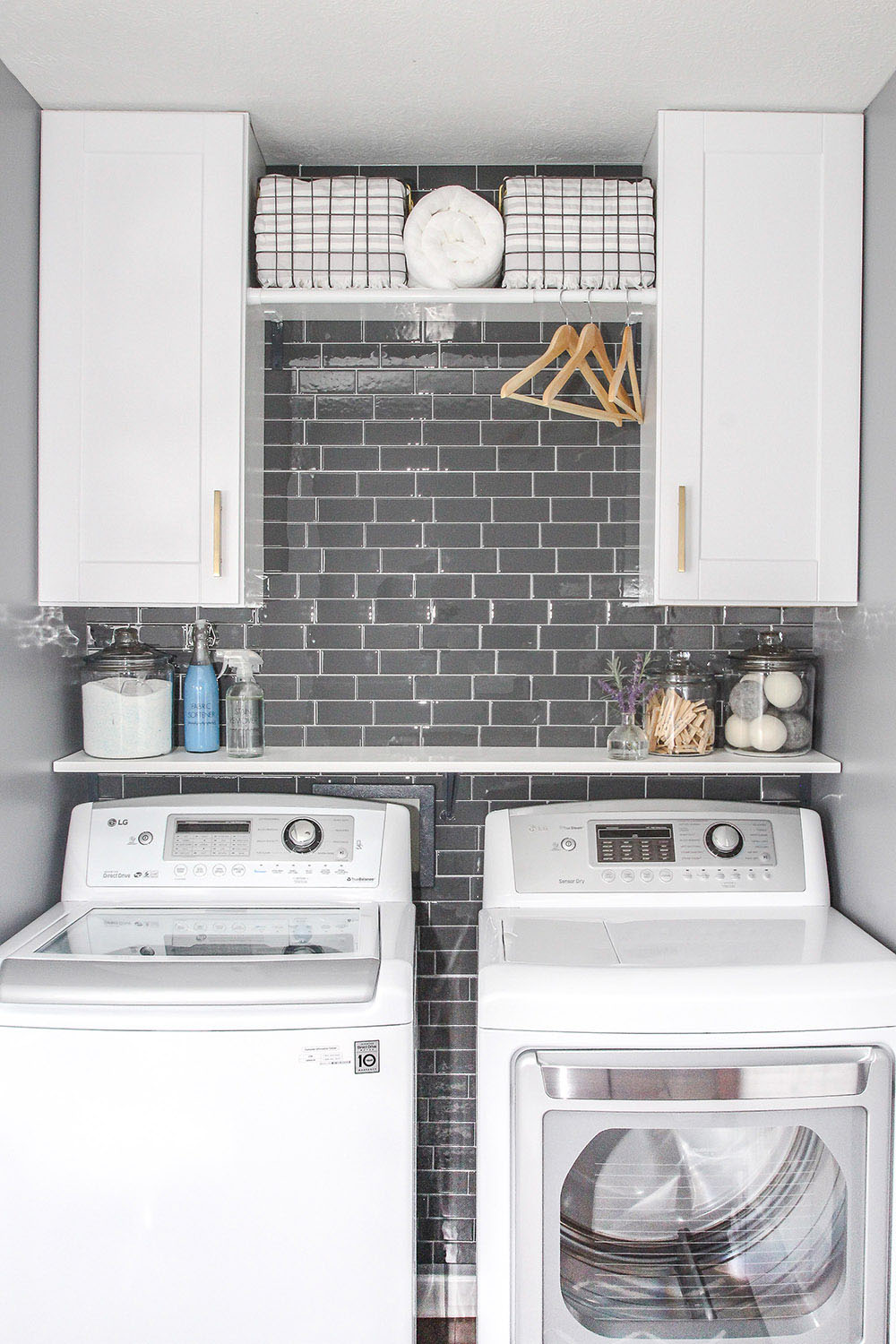 A laundry room decorated in gray and white with white laundry appliances.