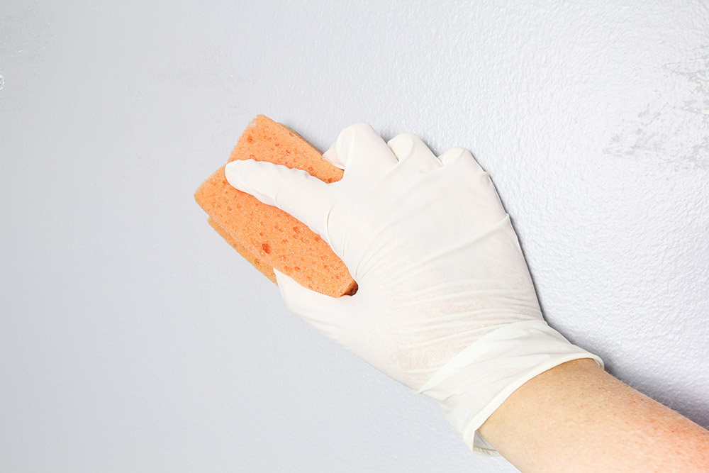 A person wearing gloves to wipe down a wall with a sponge and TSP.