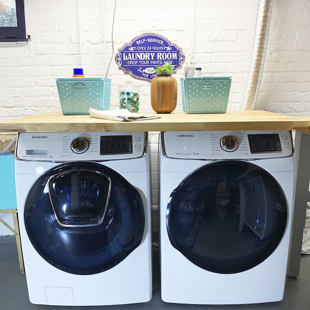 A Samsung white front load washing machine and dryer with a butcher block counter on top.
