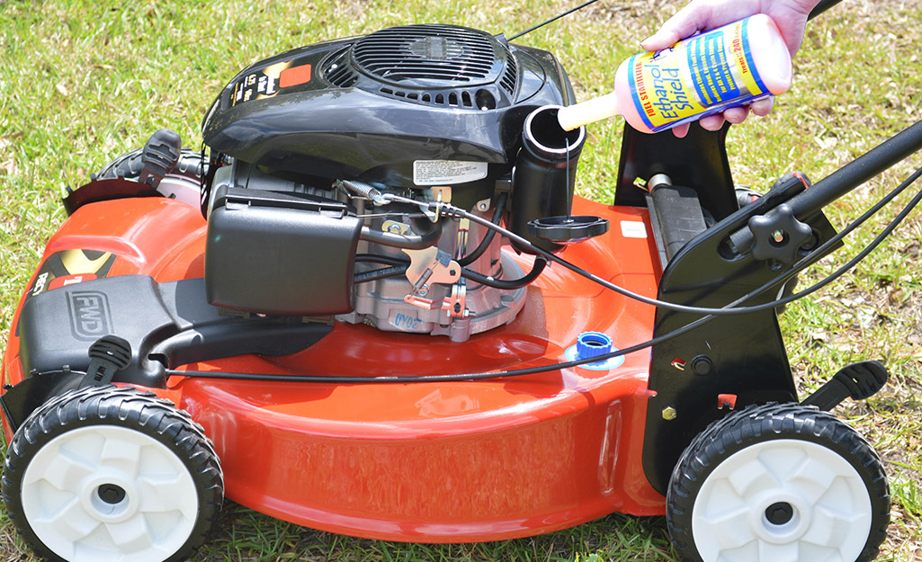 Someone pouring fuel cleaner in a lawn mower engine.