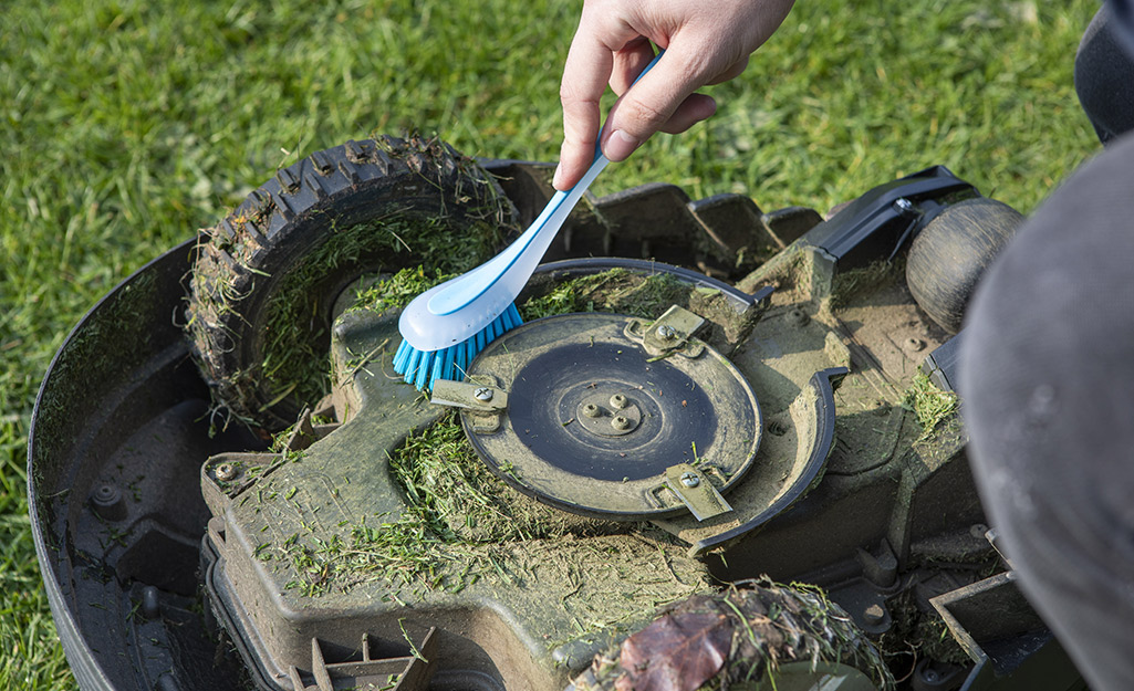 Someone cleaning around the blade of a mower.