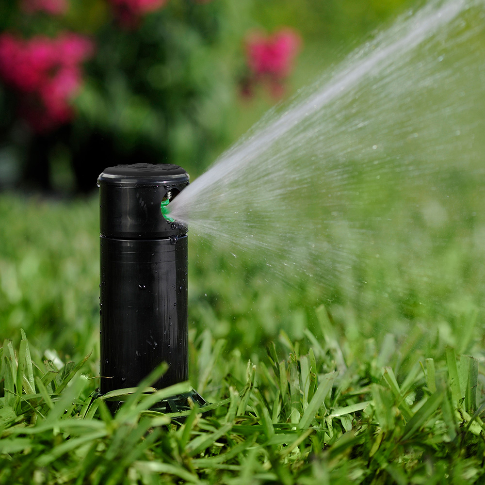 A fixed head sprinkler sprays water over a lawn and garden.