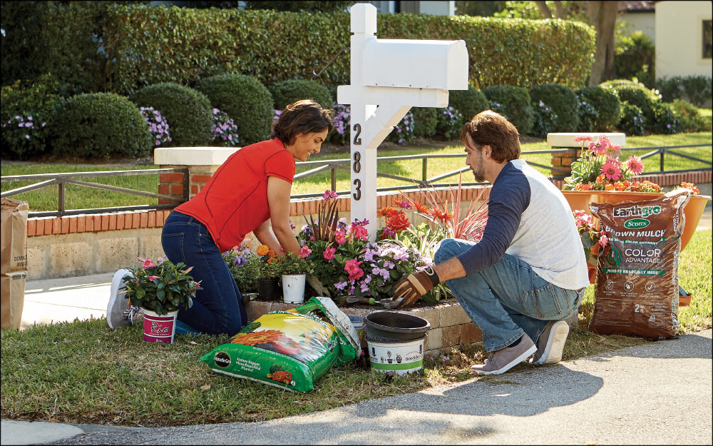 Couple planting flowers around a post mail box.