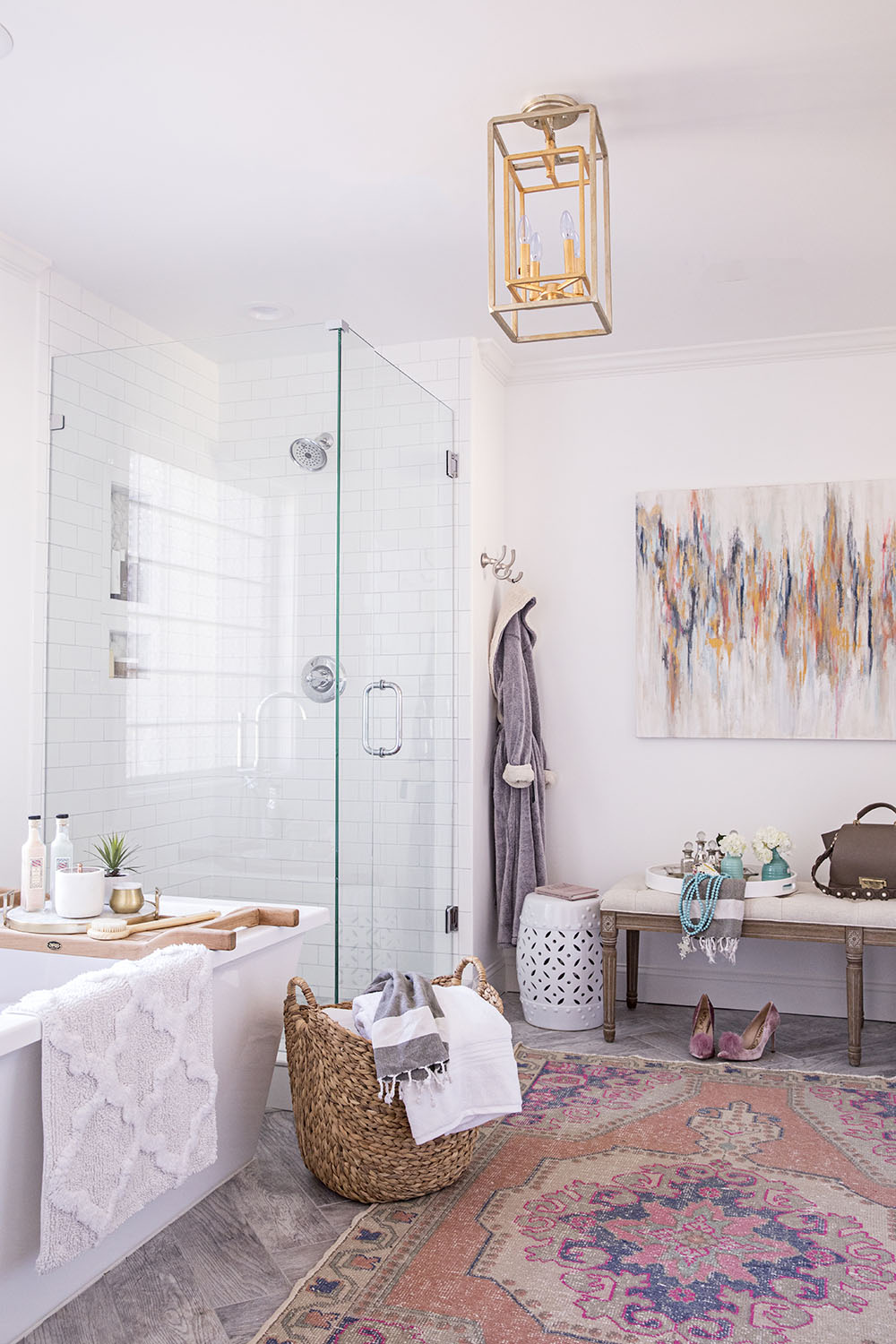 A master bathroom decorated with a large rug, artwork, and gold light fixture.
