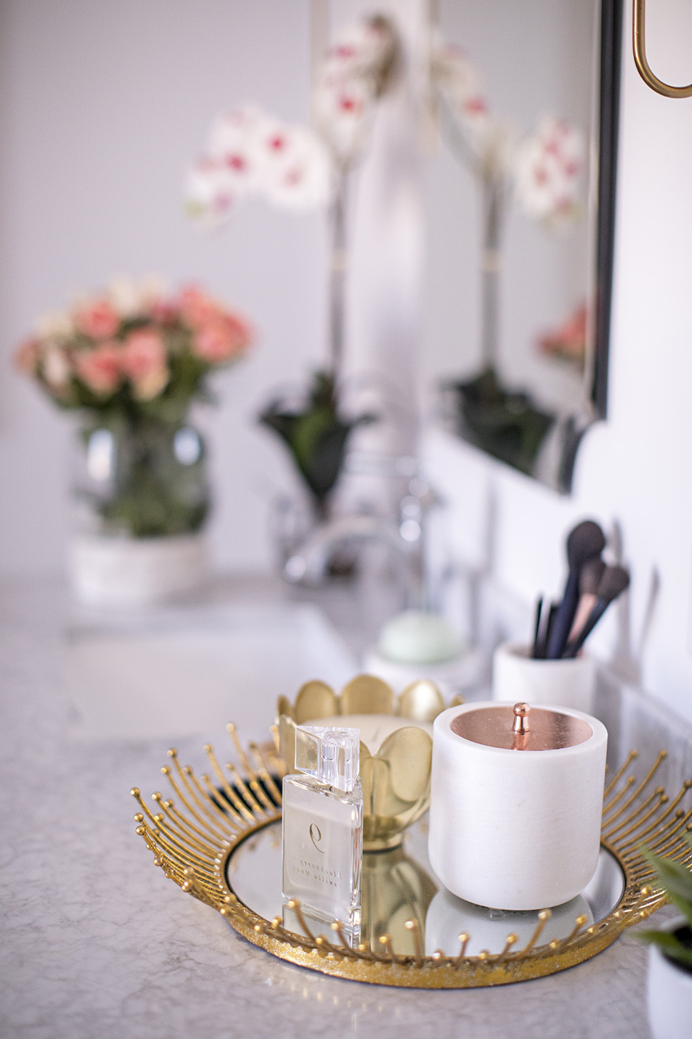 A decorated gold and mirrored tray sit on a marble vanity top.