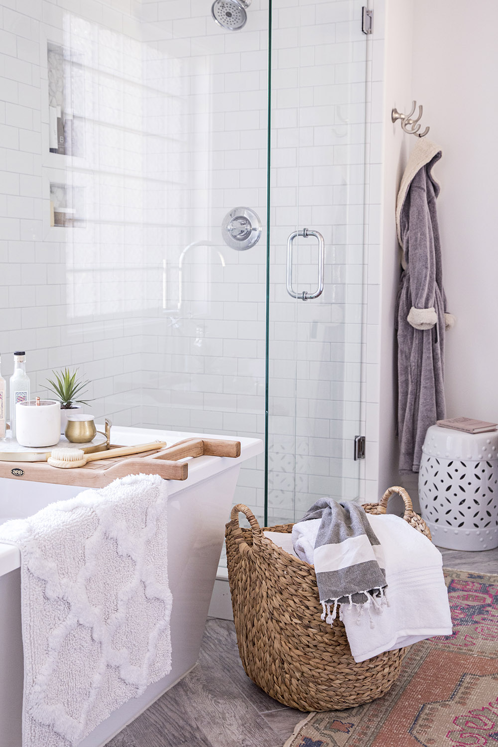 A freestanding bathtub in front of a white tiled shower with glass doors.