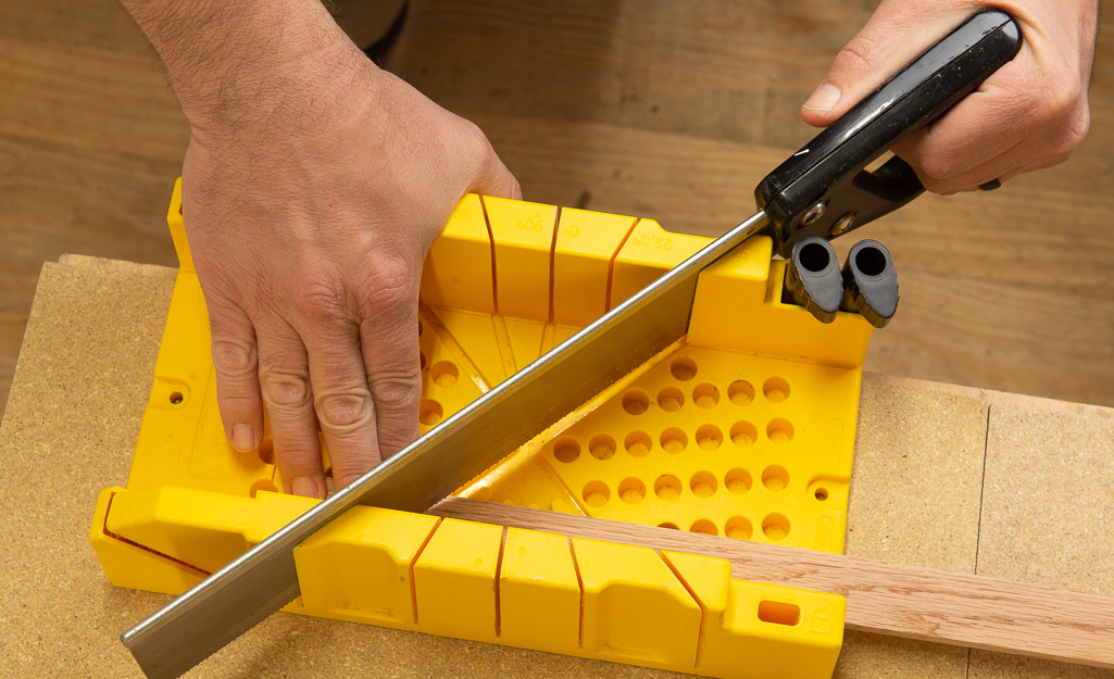 A man using a yellow guide to cut moulding. A man using a yellow guide to cut moulding.