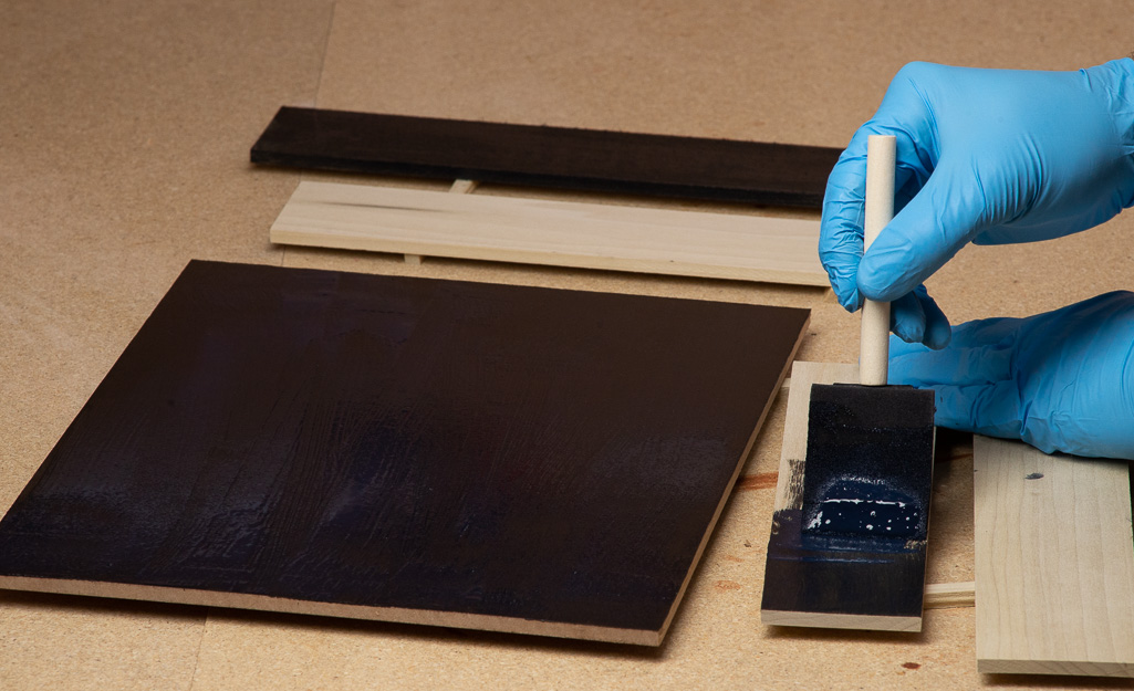 A person painting the back of a display case in black. A person painting the back of a display case in black.