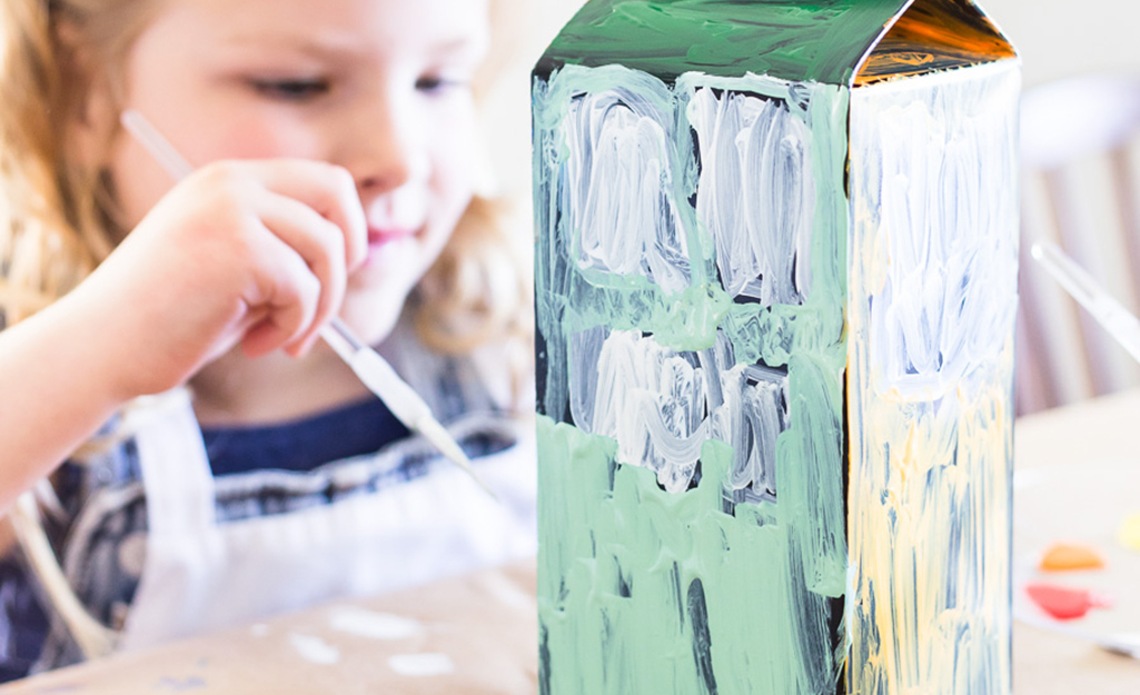 A young girl painting a design on a milk carton.