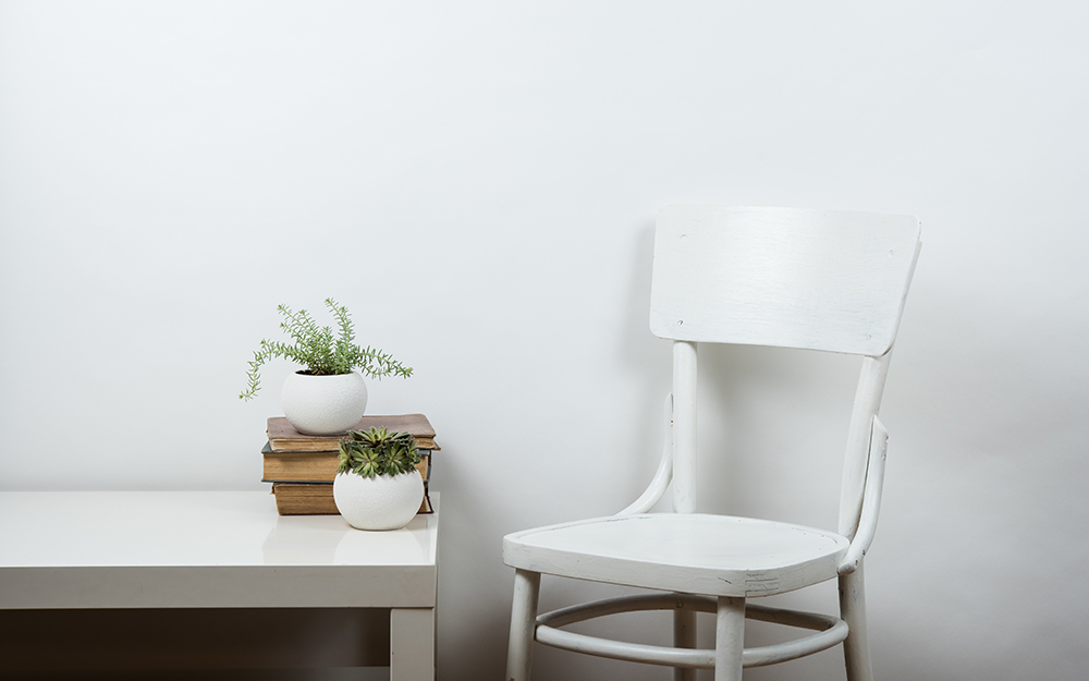 A white chair next to a white table with a plants on it.