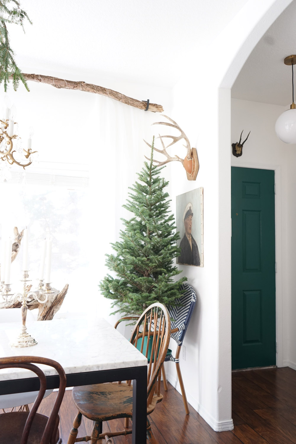 A small undecorated Christmas tree sits in a chair behind a dining table.