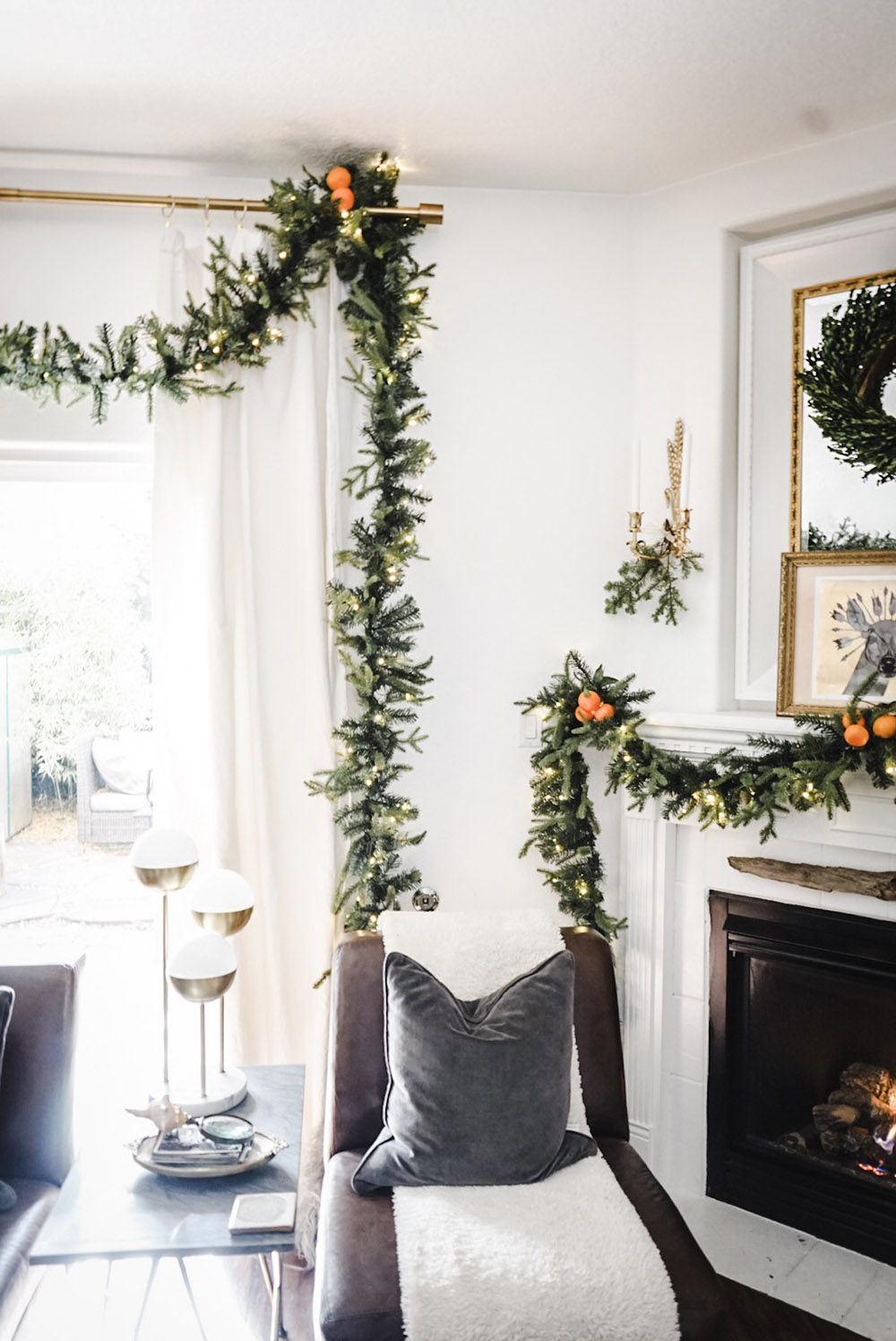 A window and fireplace decorated with garland and oranges.
