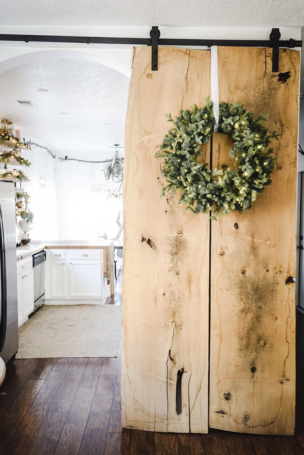 A wooden door on barndoor hardware is decorated with a wreath.