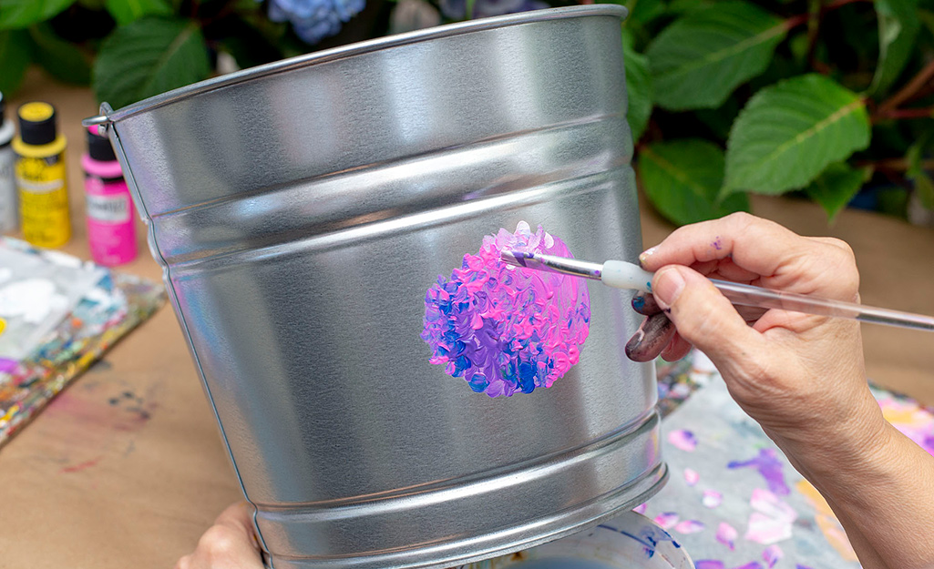 A person adding white paint to a galvanized bucket.