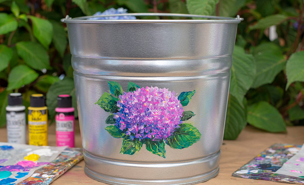 A galvanized bucket with a painted hydrangea on it.
