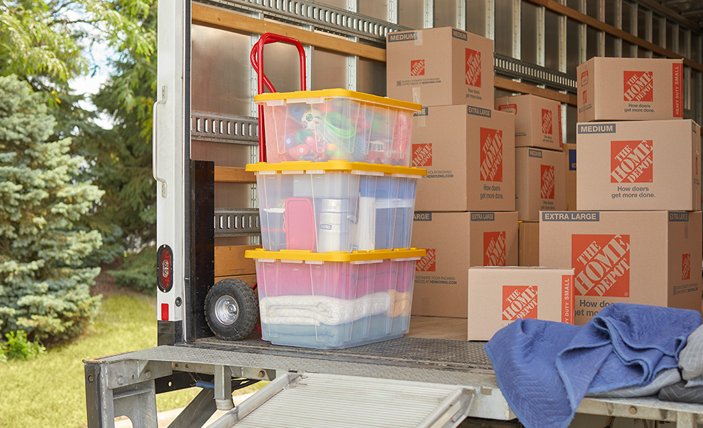 A group of moving boxes filling up a moving truck in front of a house.