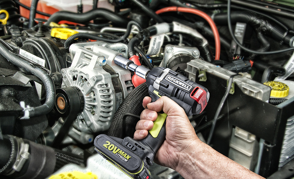 A hand using a power tool under the hood of a vehicle
