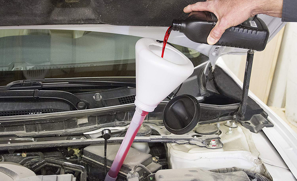 A hand pouring oil into a funnel under the hood of a car A hand pouring oil into a funnel under the hood of a car