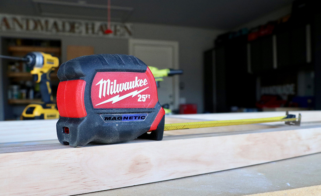 A tape measure sits on a piece of lumber in a garage.