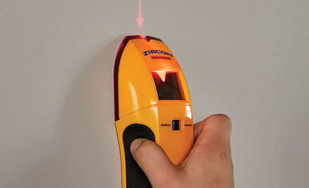 A person uses a stud finder on a wall. 