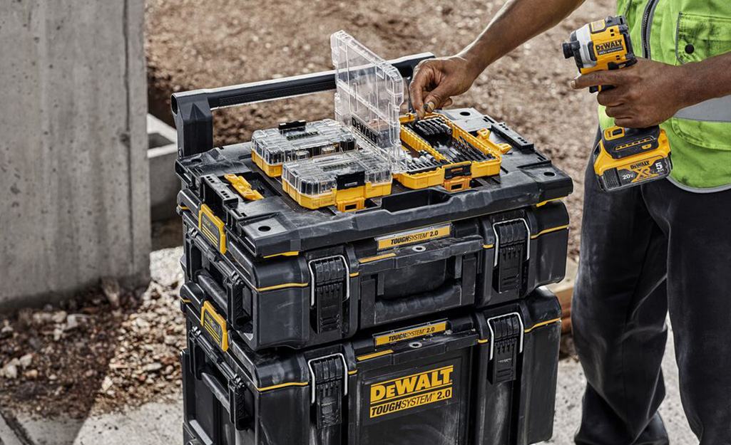 A man takes a drill bit out of case rests on a stack of tool boxes.
