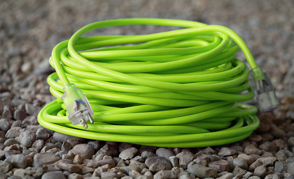 A coiled green extension cord rests on gravel.