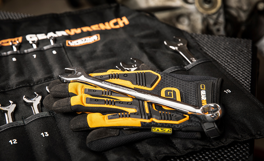 A wrench lays on top of a pair of work gloves and a case holding a set of wrenches.