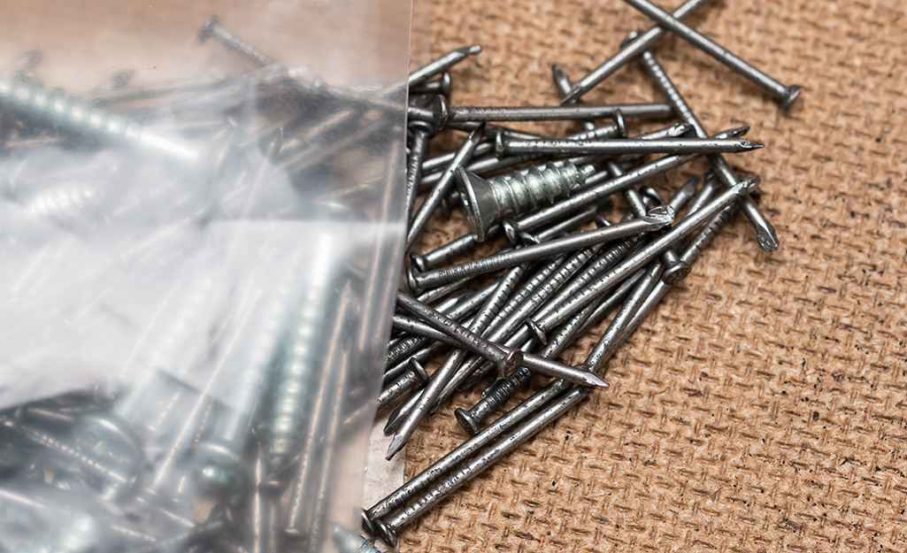 Various nails and screws are scattered on a textured surface.