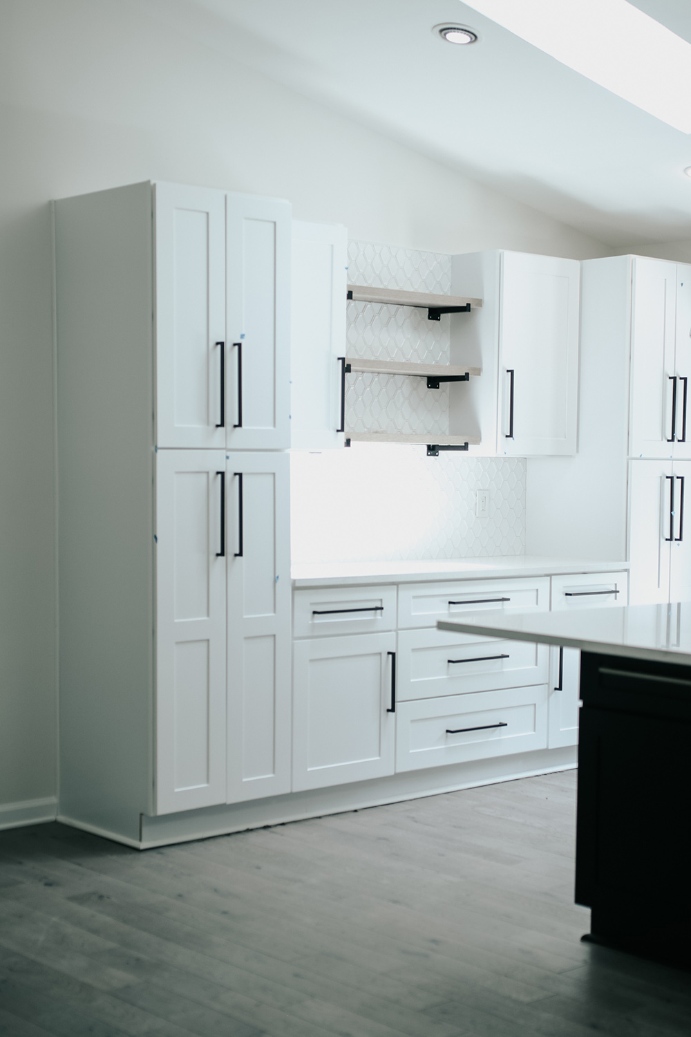A kitchen with light hardwood floors and white shaker cabinets with large black hardware. A kitchen with light hardwood floors and white shaker cabinets with large black hardware.