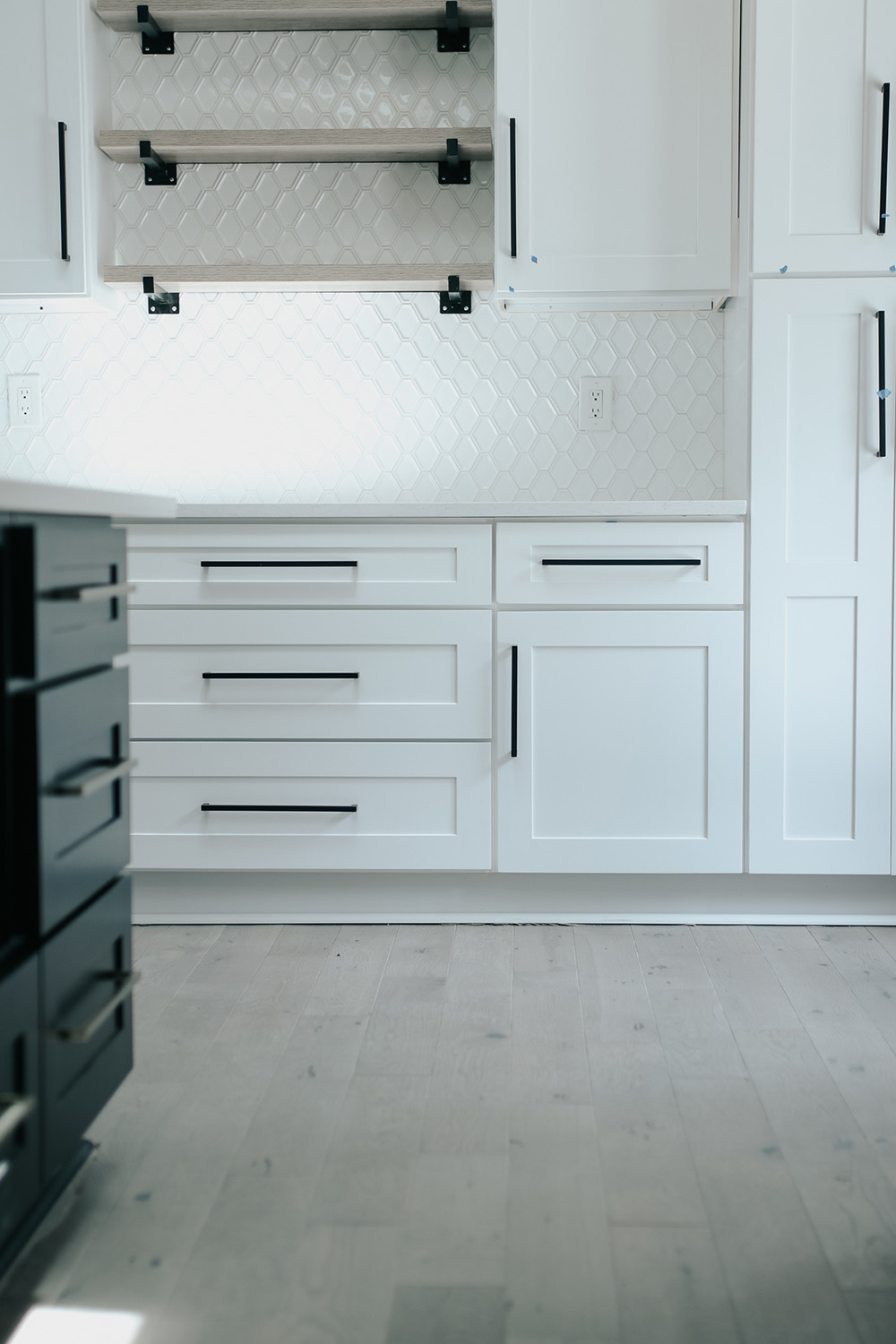 A kitchen with white cabinets, open shelving, and light hardwood floors. A kitchen with white cabinets, open shelving, and light hardwood floors.