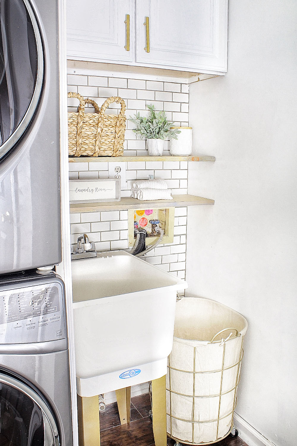 A small laundry room sink with gold legs and a wire and canvas laundry basket.