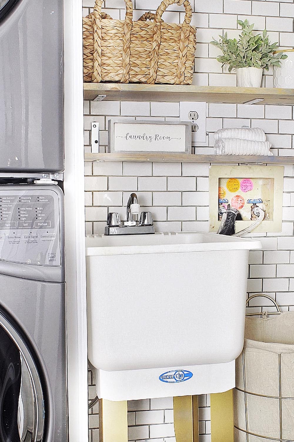 A small laundry room sink with gold painted legs sits in front of a white tile wall.