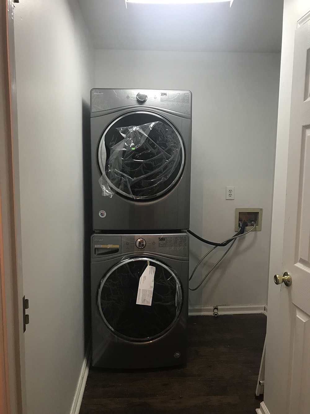 A stacked Whirlpool washer and dryer sit in an empty laundry room.
