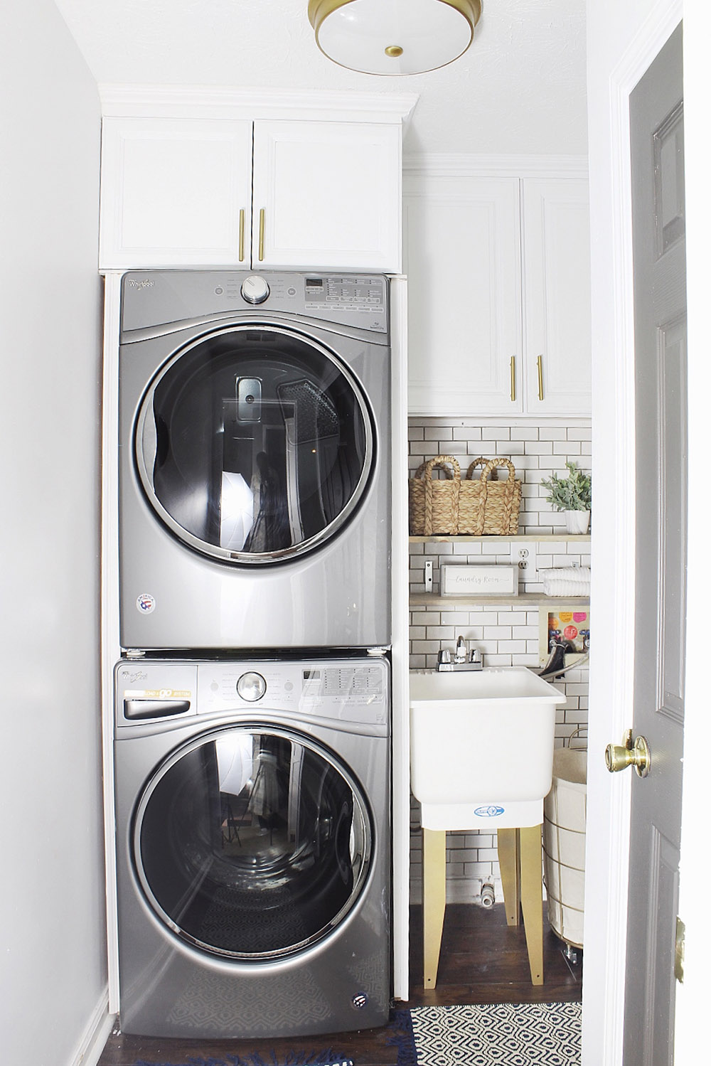 An updated laundry room with white cabinets, gold hardware, and a new washer and dryer.